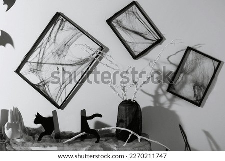Black frames with cobweb on white wall and different Halloween decor on fireplace indoors