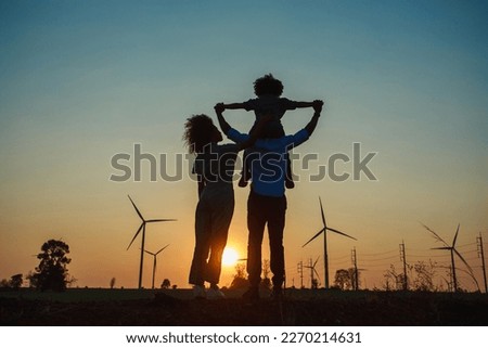 Silhouettes of Happy family father, mother and child daughter for hand and looking on windmill field at sunrise.windmills for electricity generation at sunrise by producing sustainable energy Concept,