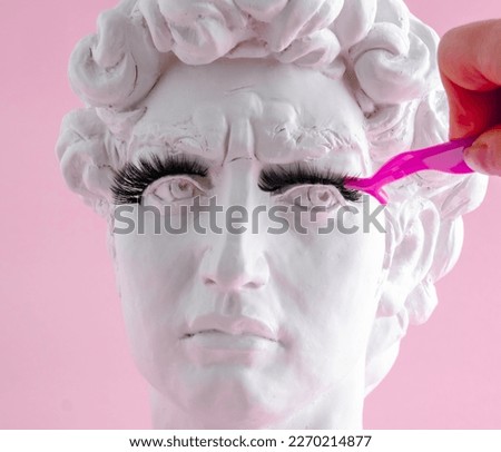 Plaster statue head wearing eyelashes pink background. Beauty procedure concept.