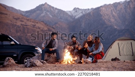 Students on a trip - four hipster multiethnic friends spending their time together, sitting near bonfire, chatting, roasting marshmallows and listening to guitar music - friendship concept  Royalty-Free Stock Photo #2270218481