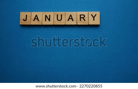 The word January is made of wooden cubes on a blue background. Winter month. Top view