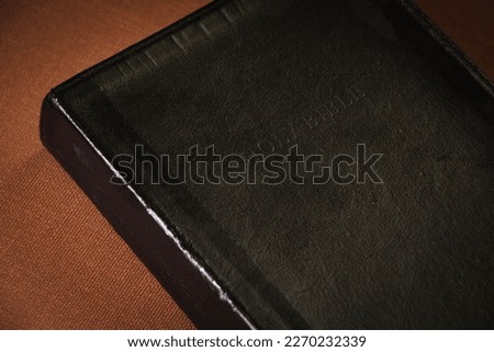 Holy Bible, black cover, brown background. Gold letters.