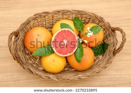 Wicker basket with fresh ripe grapefruits and green leaves on wooden table, top view