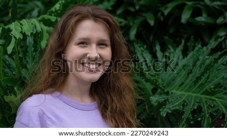 Portrait of young woman standing on an ivy, fern wall or in greenery, breathing, smiling and looking away girl relaxing outdoors at summer day.Love for nature, eco life,green leaves, green park