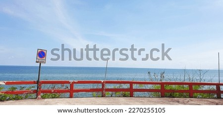 No parking sign in Thai at a red fence with blue ocean and sky as background
