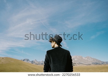 Young man in a hat against the backdrop of mountains and sky. Back view. Portrait