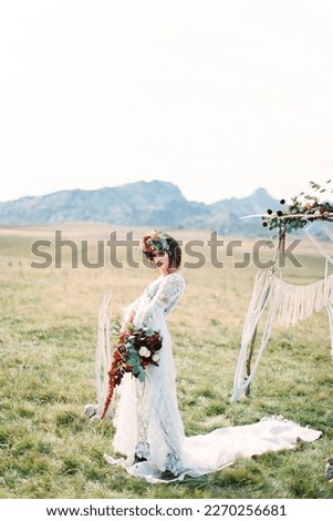 Bride in a wreath with a bouquet stands on a white carpet near a wedding arch