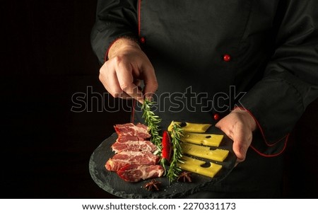 The chef puts rosemary on a plate with sliced ham and cheese. The concept of serving dishes to order by a waiter with a place for advertising on a black background