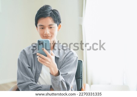 Young man sitting on a sofa operating a smartphone Royalty-Free Stock Photo #2270331335