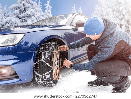 Putting winter chains on car. Man's hands putting on snow chains on the car wheel on the icy road at winter mountains. Royalty-Free Stock Photo #2270362747