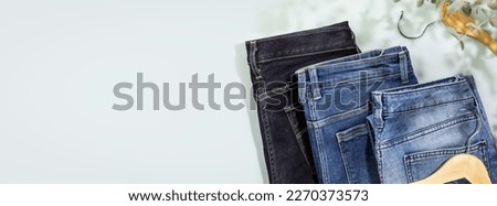 Sustainable shopping banner with different kind of jeans with wooden hangers on blue background with shadows. Denim clothing store. Spring sale. Casual wear. Flat lay, copy space, banner size Royalty-Free Stock Photo #2270373573