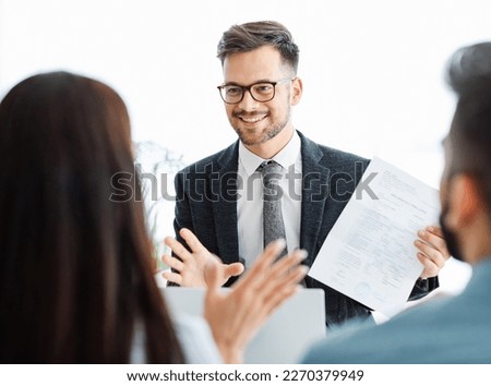 Real estate agent with couple meeting in office, Successful partnership, Confident young man businessman holding some document and pointing it while sitting together with cheerful young couple  Royalty-Free Stock Photo #2270379949