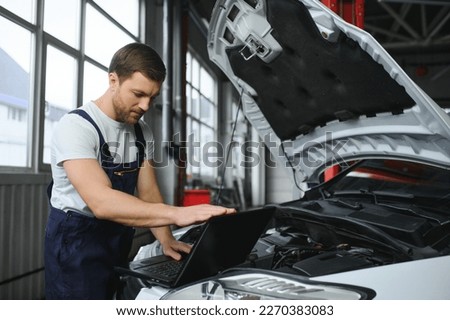 Mechanic man mechanic manager worker using a laptop computer checking car in workshop at auto car repair service center. Engineer young man looking at inspection vehicle details under car hood. Royalty-Free Stock Photo #2270383083