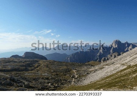 A view on a vast valley in Italian Dolomites. The valley is surrounded with high and sharp mountains from each side. Morning sun warms the valley up. Remote and isolated place. Remedy Royalty-Free Stock Photo #2270393337