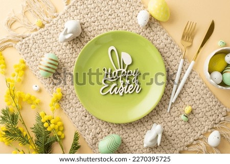Easter concept. Top view photo of green plate with inscription happy easter knife fork bowl with colorful easter eggs ceramic bunnies cloth napkin and mimosa on isolated beige background