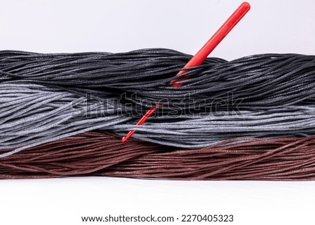 Yarn for knitting of black, gray and brown colors with red crochet. Isolated view on a white background.