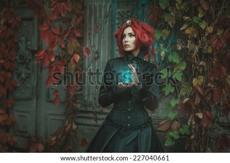 Fabulous girl with red hair, she is holding an hourglass. At the door of the castle. Royalty-Free Stock Photo #227040661