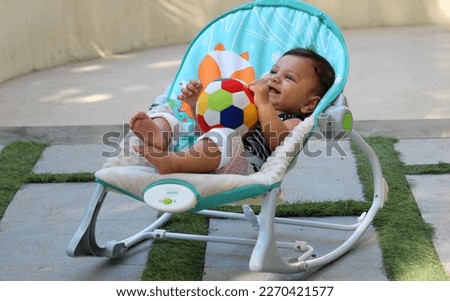A cute Indian Toddler sitting on his rolling rocker with a ball in his hand playing it and laughing fullest  Royalty-Free Stock Photo #2270421577