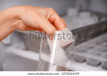 The girl collects frozen ice cubes in a glass goblet from the freezer. Royalty-Free Stock Photo #2270424199