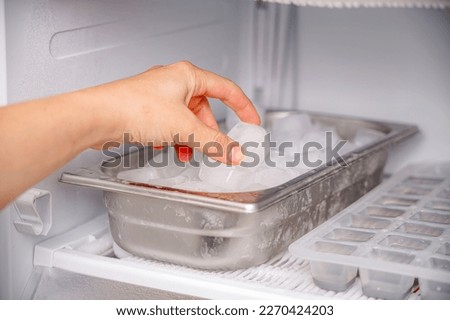 The girl collects frozen ice cubes from the freezer to prepare soft drinks. Royalty-Free Stock Photo #2270424203
