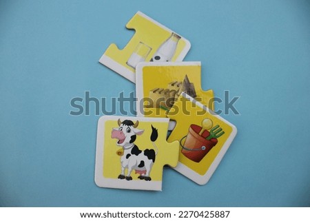 Educational puzzles with pictures of milk, sand, sand bucket and cow scattered scattered on a blue background.