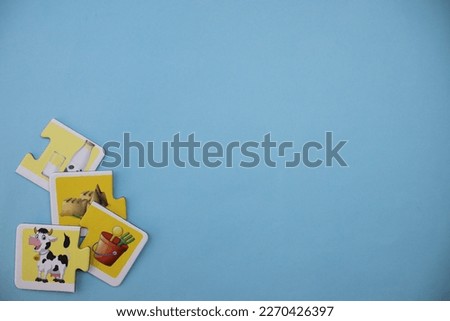 Educational puzzles with pictures of milk, sand, sand bucket and cow scattered scattered on the lower left of the blue background.