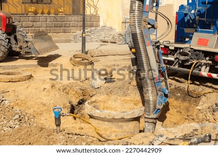 Workers use a suction excavator based on a truck to sample soil in a well for communications during restoration work on a street. Royalty-Free Stock Photo #2270442909