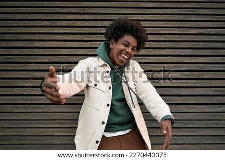 Happy funky funny generation z hipster rapper African American guy dancing, singing, having fun feeling hip-hop or rap vibe, moving and gesturing standing at wooden wall outdoors. Royalty-Free Stock Photo #2270443375