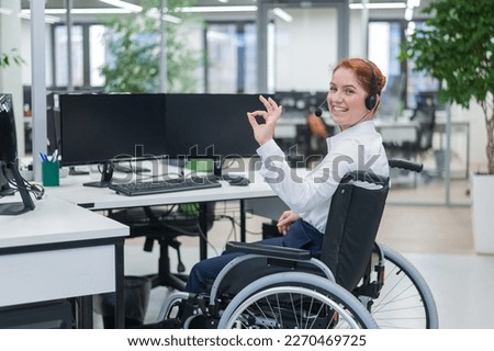 Caucasian woman in wheelchair showing ok sign while sitting in open space office.