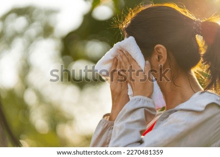 Asian woman in sportswear wiping sweat on her face with towel during jogging exercise at public park at summer sunset. Healthy girl enjoy outdoor lifestyle sport training workout running in the city. Royalty-Free Stock Photo #2270481359