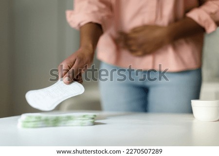 African american woman feeling pain during menstrual cycle and taking daily sanitary pad from table, selective focus, closeup, free space