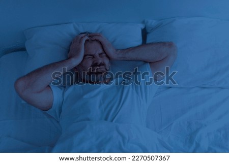 Top view of unhappy grey-haired bearded mature man wearing pajamas lying in bed, touching his head, suffering from headache or migraine at night, copy space Royalty-Free Stock Photo #2270507367