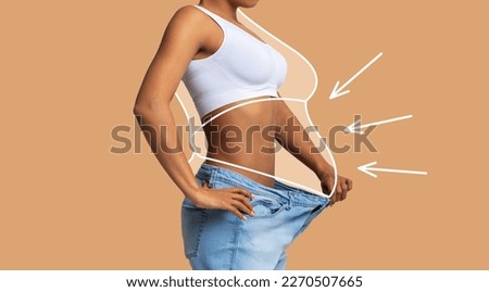 Young slim african american female in big jeans enjoy weight loss result with fat abstract body around, arrows isolated on beige wall background, studio. Diet, health and body care, before and after Royalty-Free Stock Photo #2270507665