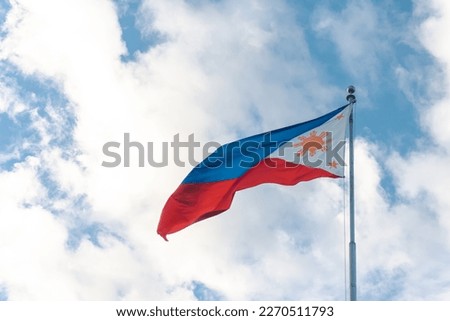 waving philippine flag in a pole with clouds and blue sky background