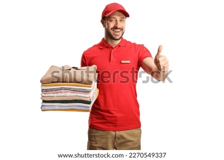 Laundry worker holding a pile of folded clothes and gesturing thumbs up isolated on a white background

