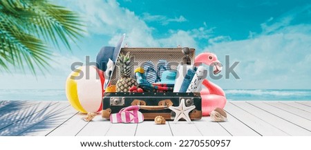 Vintage suitcase with colorful summer accessories at the tropical beach on the deck, summer vacations concept, copy space