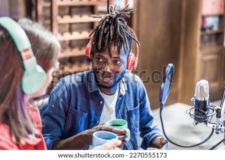 Two young men sit at a table, chatting and sipping coffee while wearing headsets and broadcasting their conversation live. The ambiance is relaxed and casual, with a comfortable and modern vibe Royalty-Free Stock Photo #2270555173