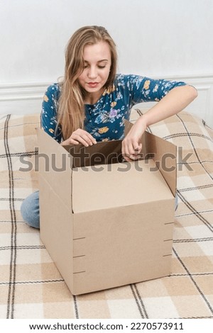 Woman sitting on bed unpacking cardboard box at home. Delivering parcel