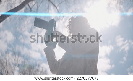 Beautiful woman with professional photo camera enjoying sunny day on a blue sky background. Action. Happy woman with curly hair walking with camera in nature outdoors.