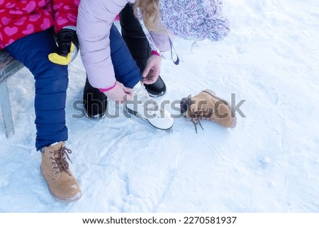 A woman helps a child put on skates and tie shoelaces, parental care.