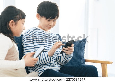 Asian little girl and boy using smart phone in living room. Royalty-Free Stock Photo #2270587677