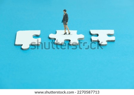 Miniature people toy figure photography. A businesswoman standing above three piece puzzle jigsaw. Isolated on blue background. Image photo