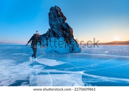 A young happy woman is skating on the transparent ice of the frozen Lake Baikal on a sunny winter day - World-famous figure skater "Polina Korobeynikova" performs on Lake Baikal