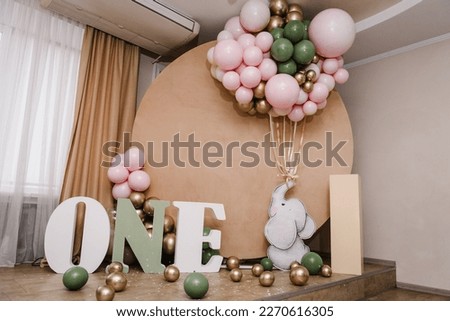 Arch decorated pink, golden, green balloons, paper decor elephant, confetti. Birthday party for 1 year old girl or boy on background brown photo wall. Reception. Celebration concept. Space for text.