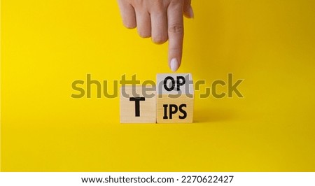 Top Tips symbol. Businessman hand points at turned wooden cubes with words Top Tips. Beautiful yellow background. Business and Top Tips concept. Copy space