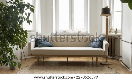 Small stylish pale sofa in modern Scandinavian interior of empty room with houseplant, torch, windows in background. Apartment flat design, real estate natural decoration. Banner shot