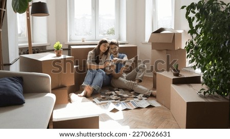 Young married couple of new homeowners selecting finishing interior materials, reviewing tile samples, using online app on tablet, discussing renovation project in new apartment with boxes