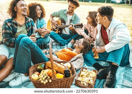 Cheerful young people having picnic party outdoors - Happy friends group having fun singing and playing guitar together - Friendship concept