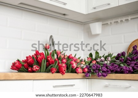 A large number of tulips of different colors lies in the kitchen in the sink. Flowers in a basket