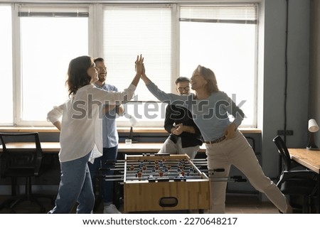 Joyful female coworkers enjoying teambuilding, recreation activity, playing table football, clapping high five hands over board game, winning battle, smiling, laughing Royalty-Free Stock Photo #2270648217